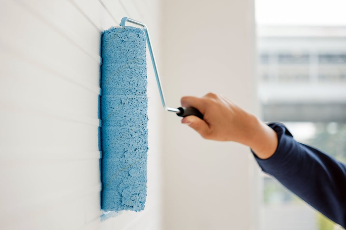 Hand applying fresh paint to an interior wall with a roller