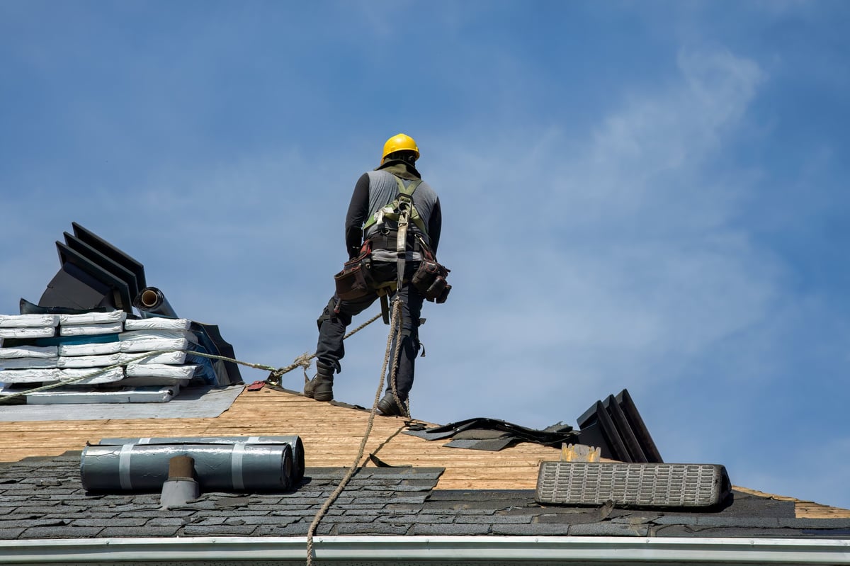 Roofer using a pneumatic nail gun to install asphalt shingles